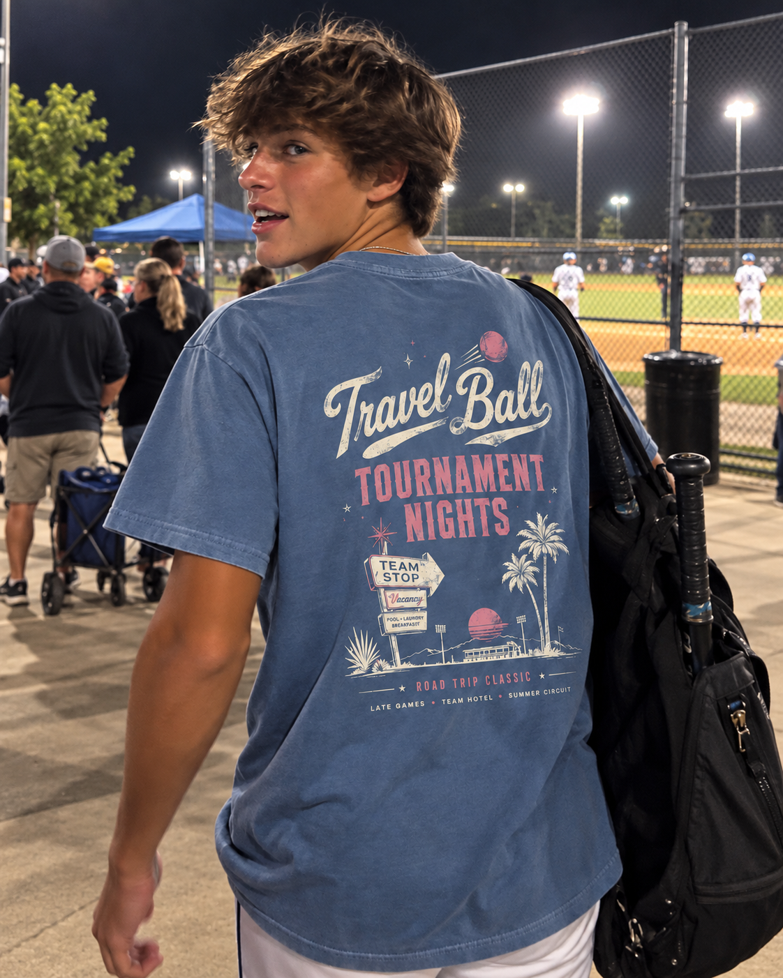 Teen boy wearing the Washed Denim adult travel ball T-shirt at a baseball field, showing the large Tournament Nights graphic on the back.